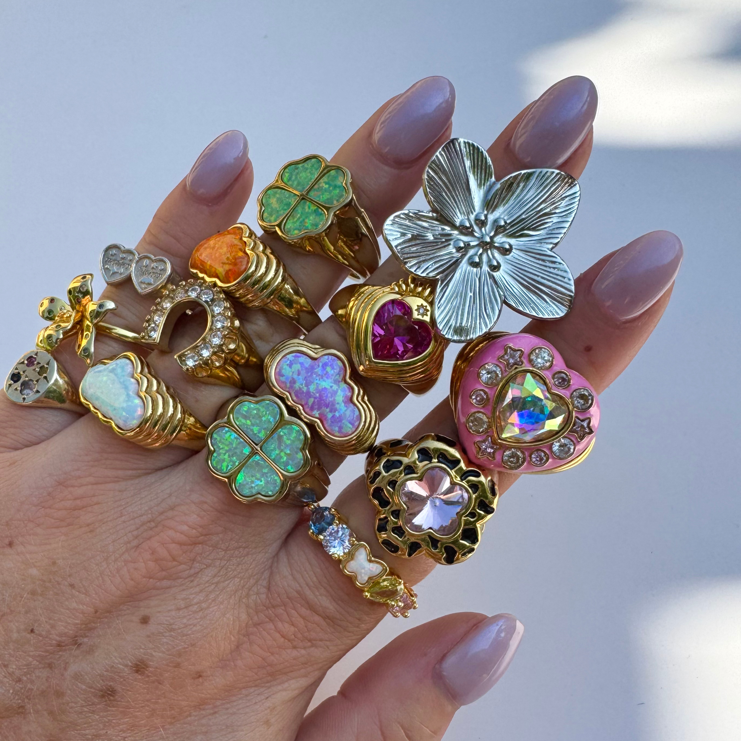 Hand wearing multiple decorative rings with various designs and colors against a neutral background