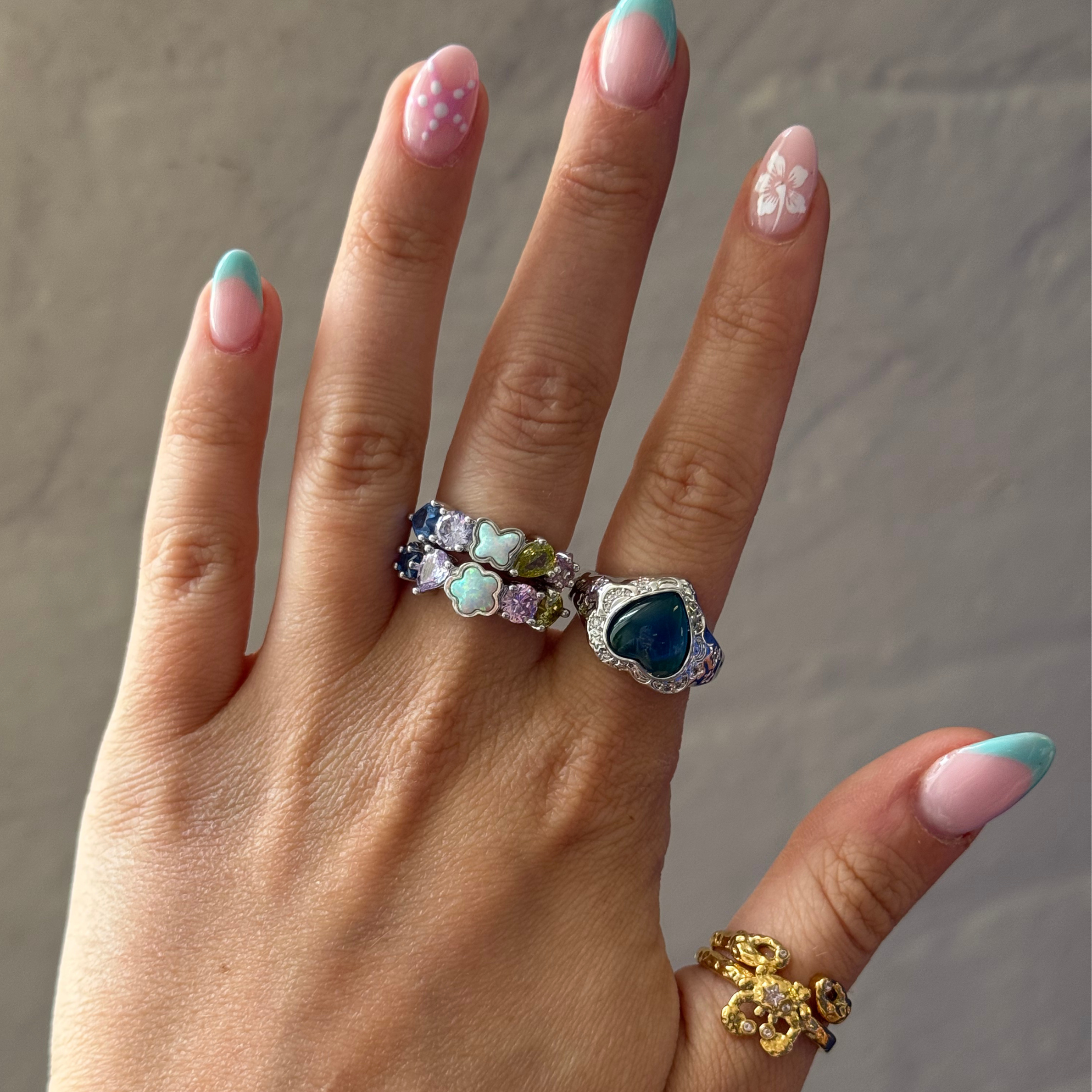 Hand wearing multiple rings with colorful gemstones against a neutral background