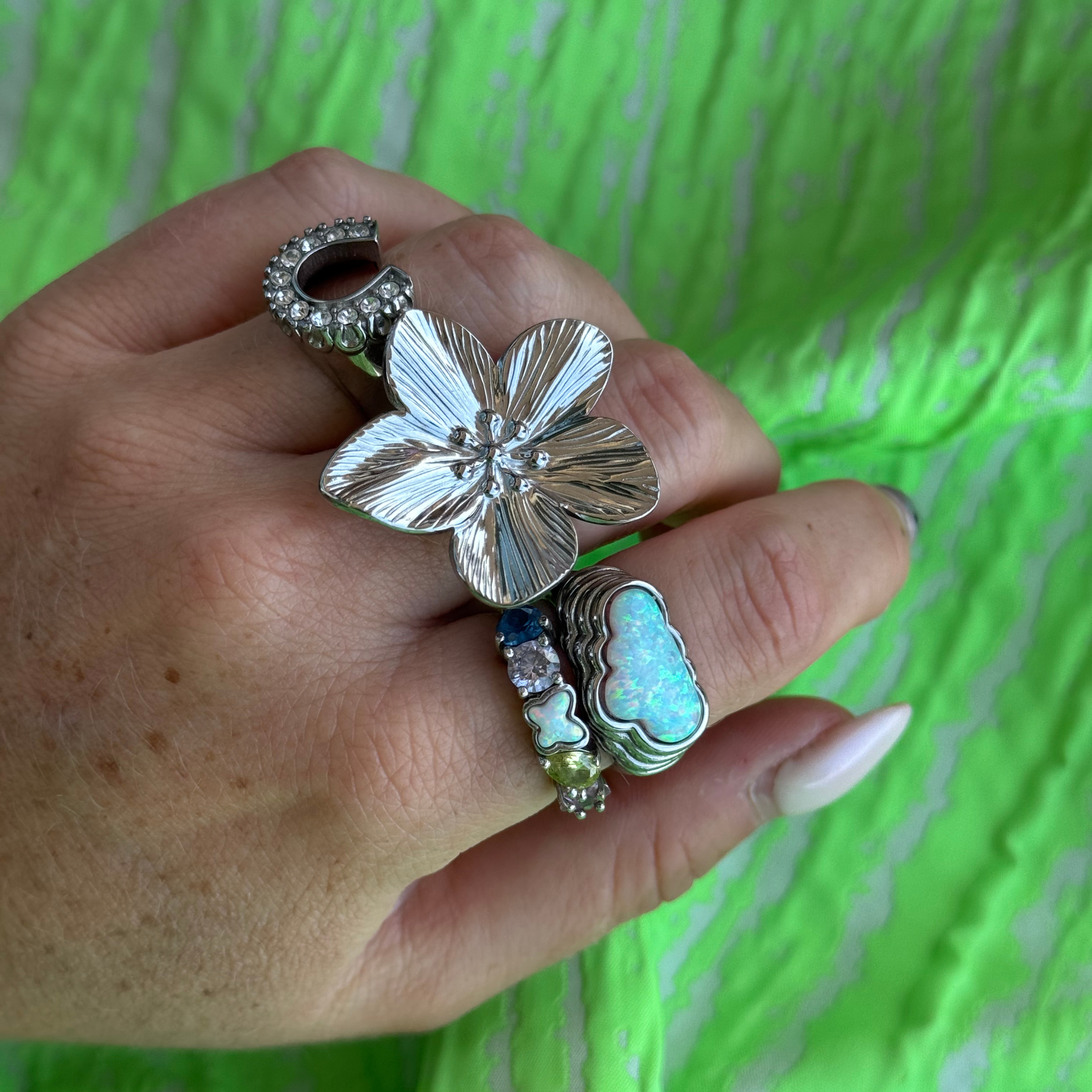 Hand wearing multiple silver rings with floral and cloud designs against a green background