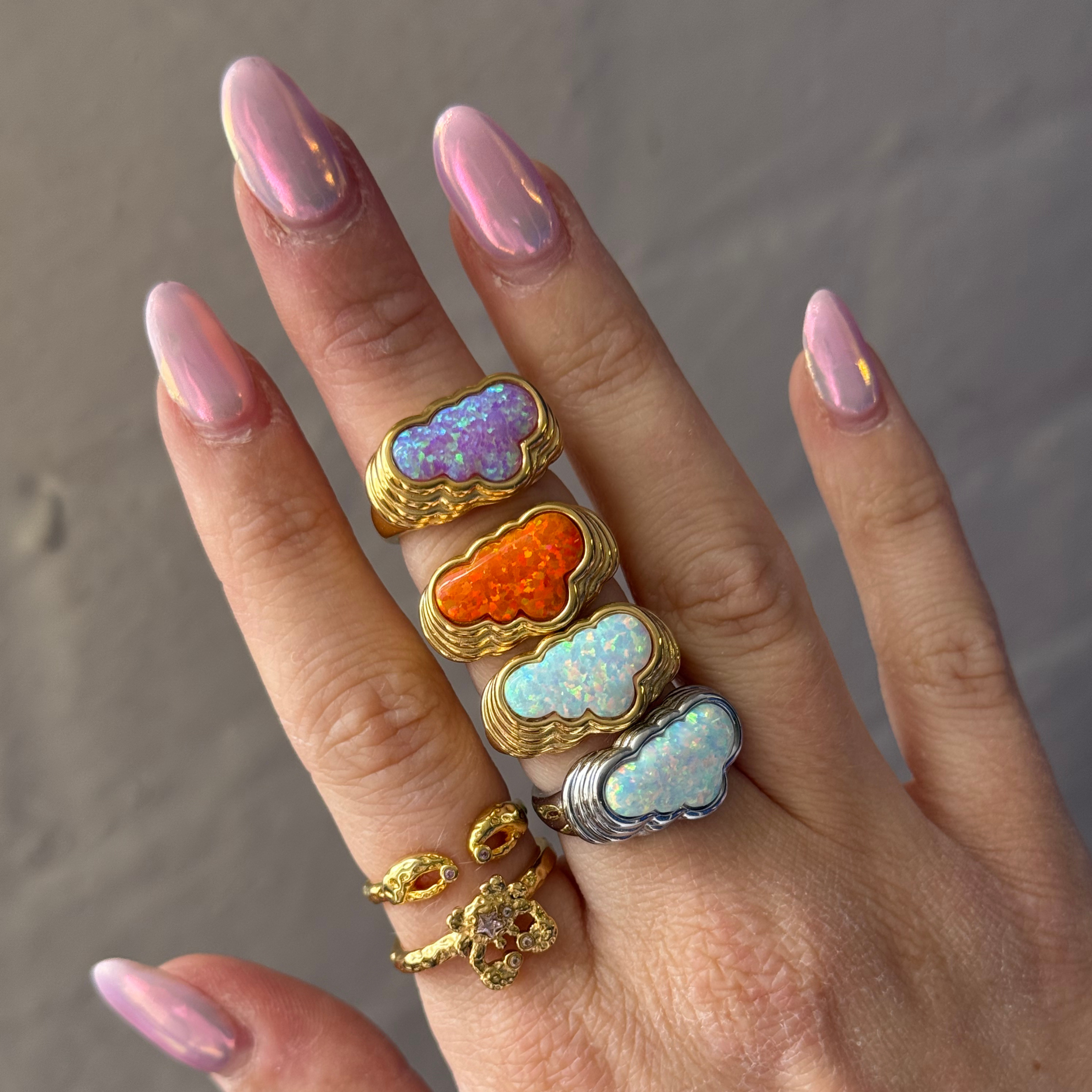 Hand wearing multiple colorful cloud-shaped rings on a neutral background