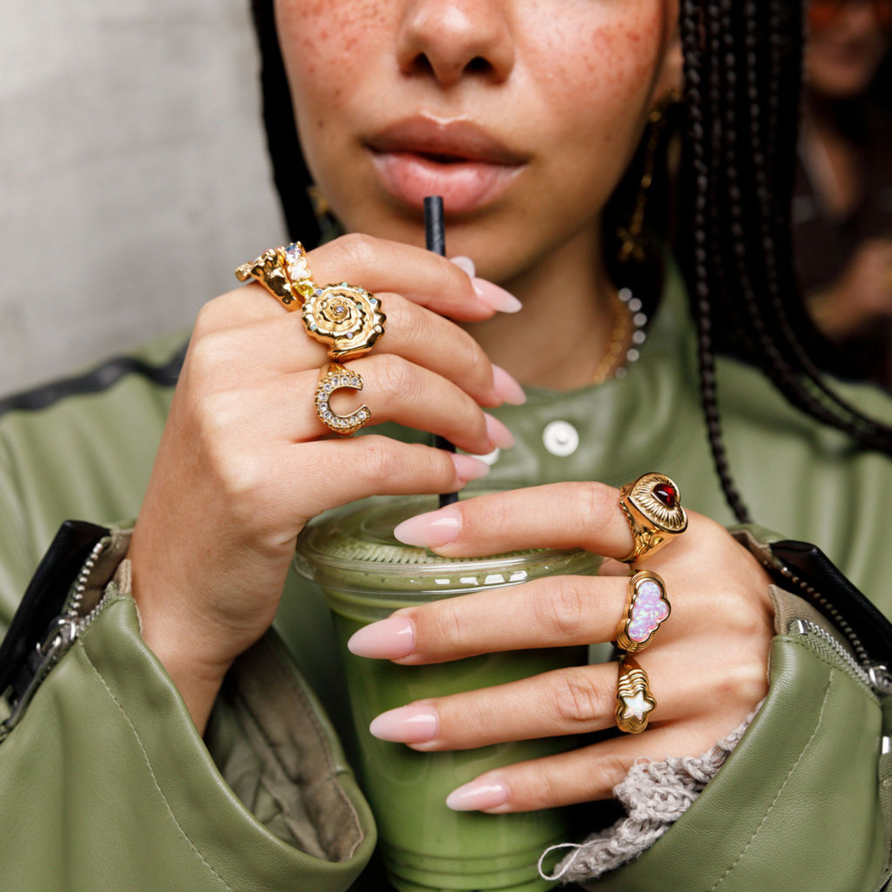Person holding a green cup with multiple rings on fingers