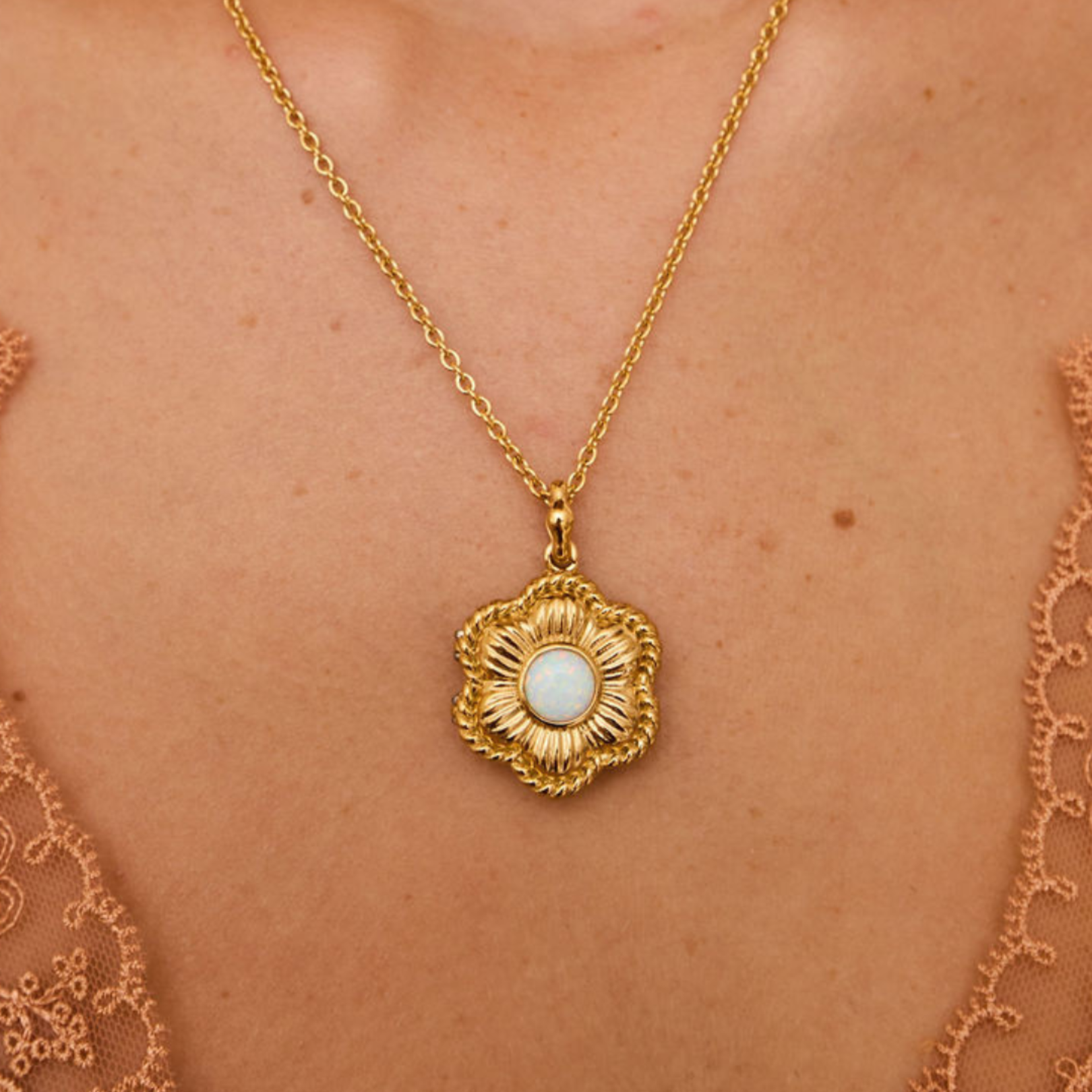 Gold necklace with a flower pendant on a person's neck.