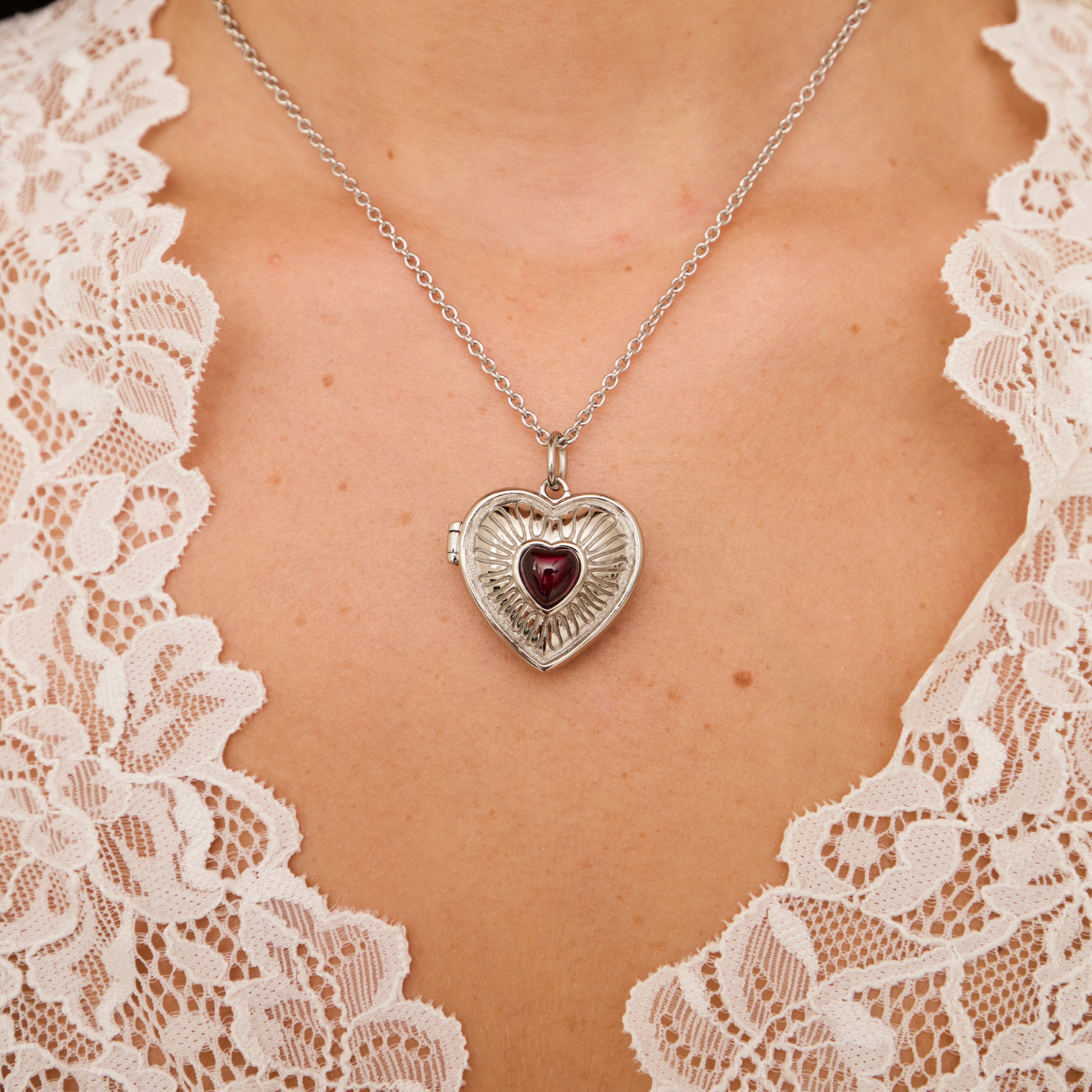 Heart-shaped locket necklace with a red gemstone on a lace garment