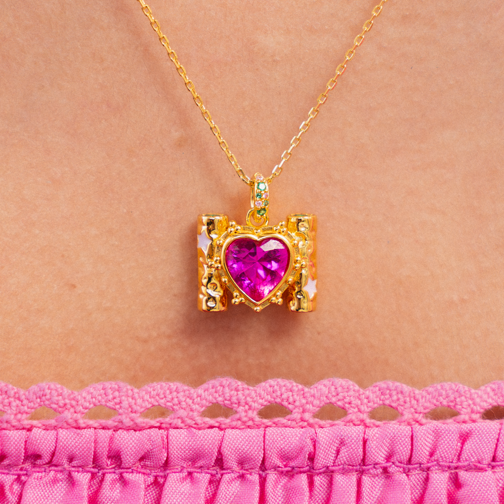 Gold necklace with a pink heart pendant on a person wearing a pink top.