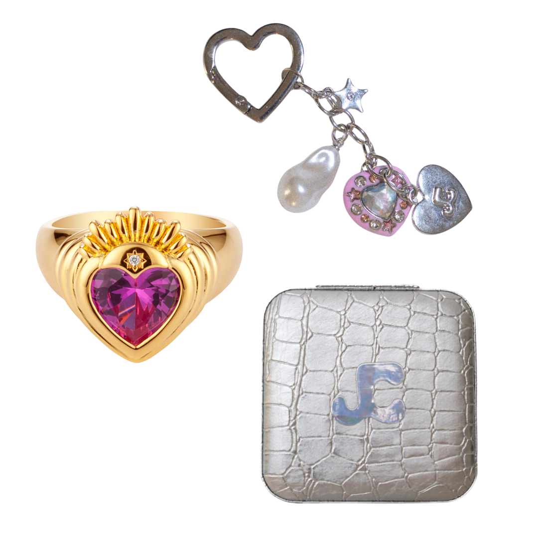 Gold heart-shaped ring with pink gem, silver keychain with charms, and silver wallet with JC logo.