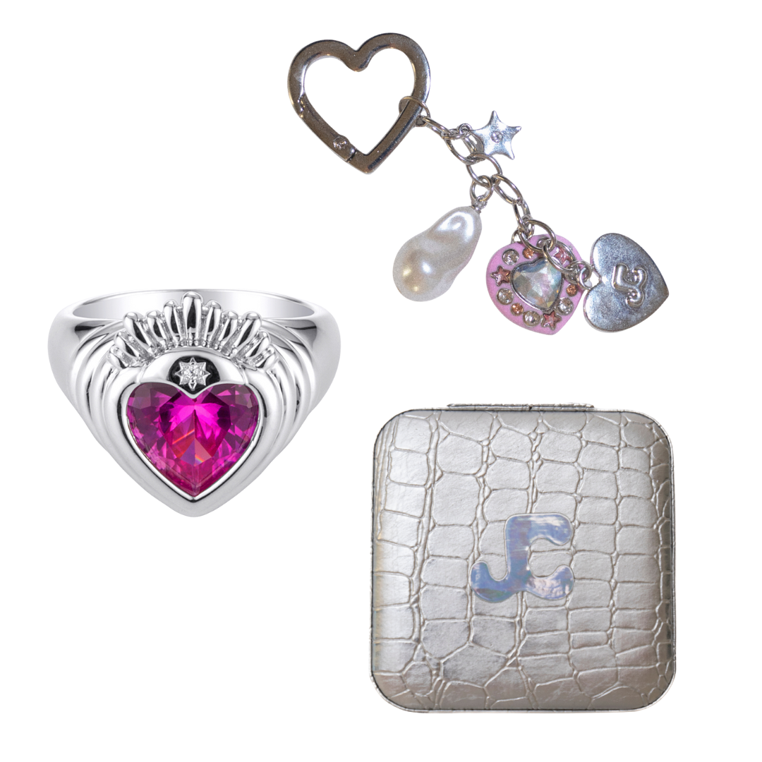 Silver heart-shaped ring with pink gem, silver keychain with charms, and silver wallet with JC logo.