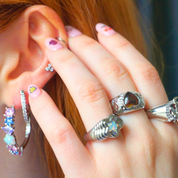 Close-up of a hand with multiple rings and earrings near an ear.