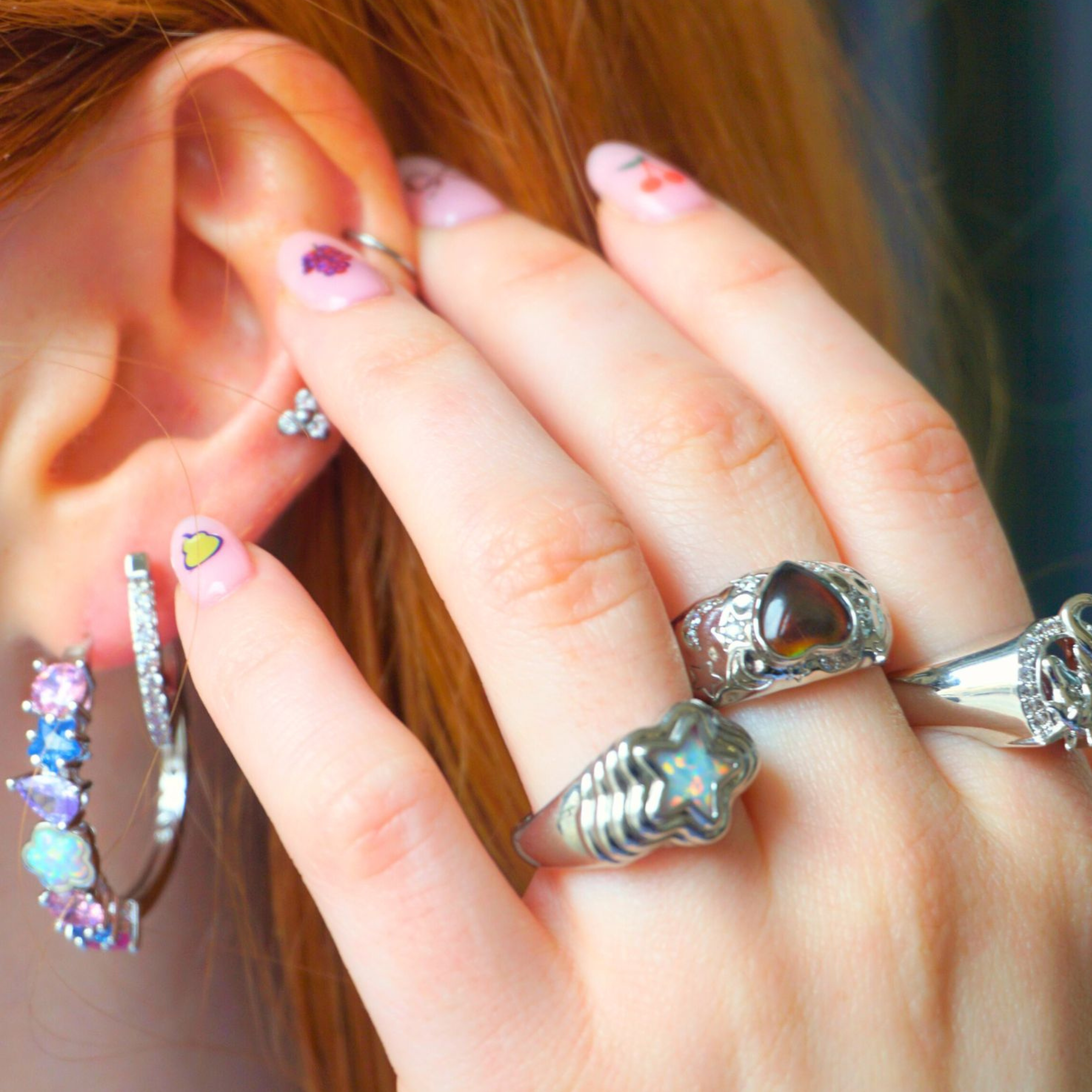 Close-up of a hand with multiple rings and earrings near an ear.