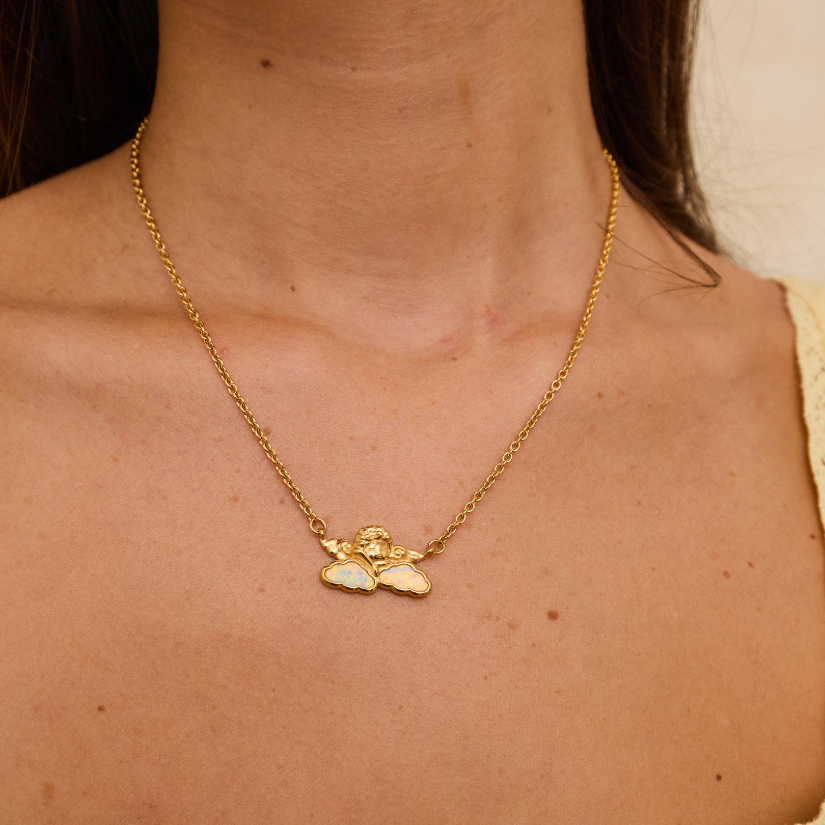 Gold necklace with a cherub pendant on a person's neck