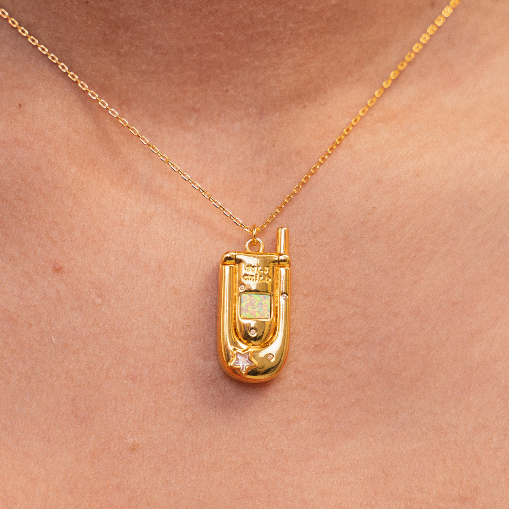 Gold necklace with a pendant shaped like an old flip phone on a person's neck.