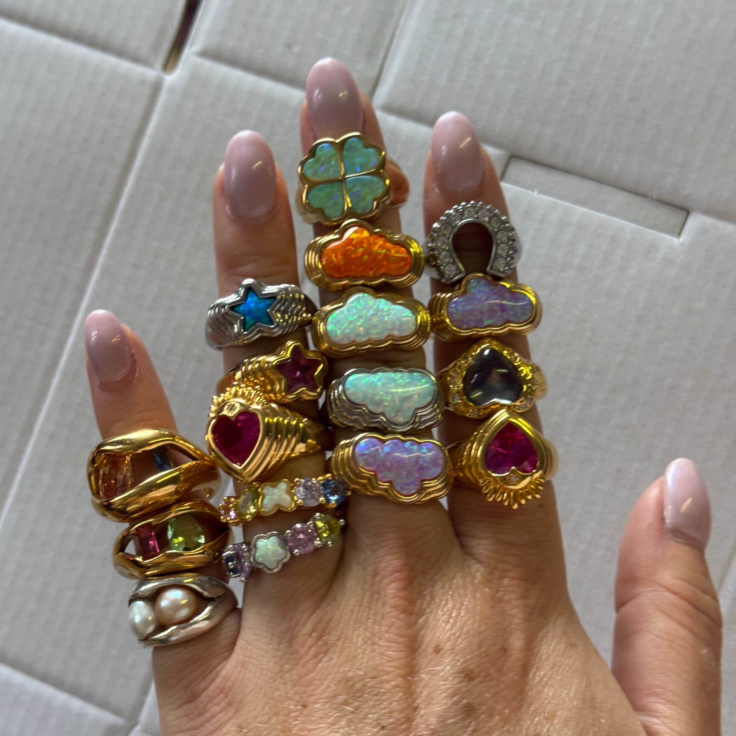 Hand wearing multiple colorful rings with various gemstones on a light background