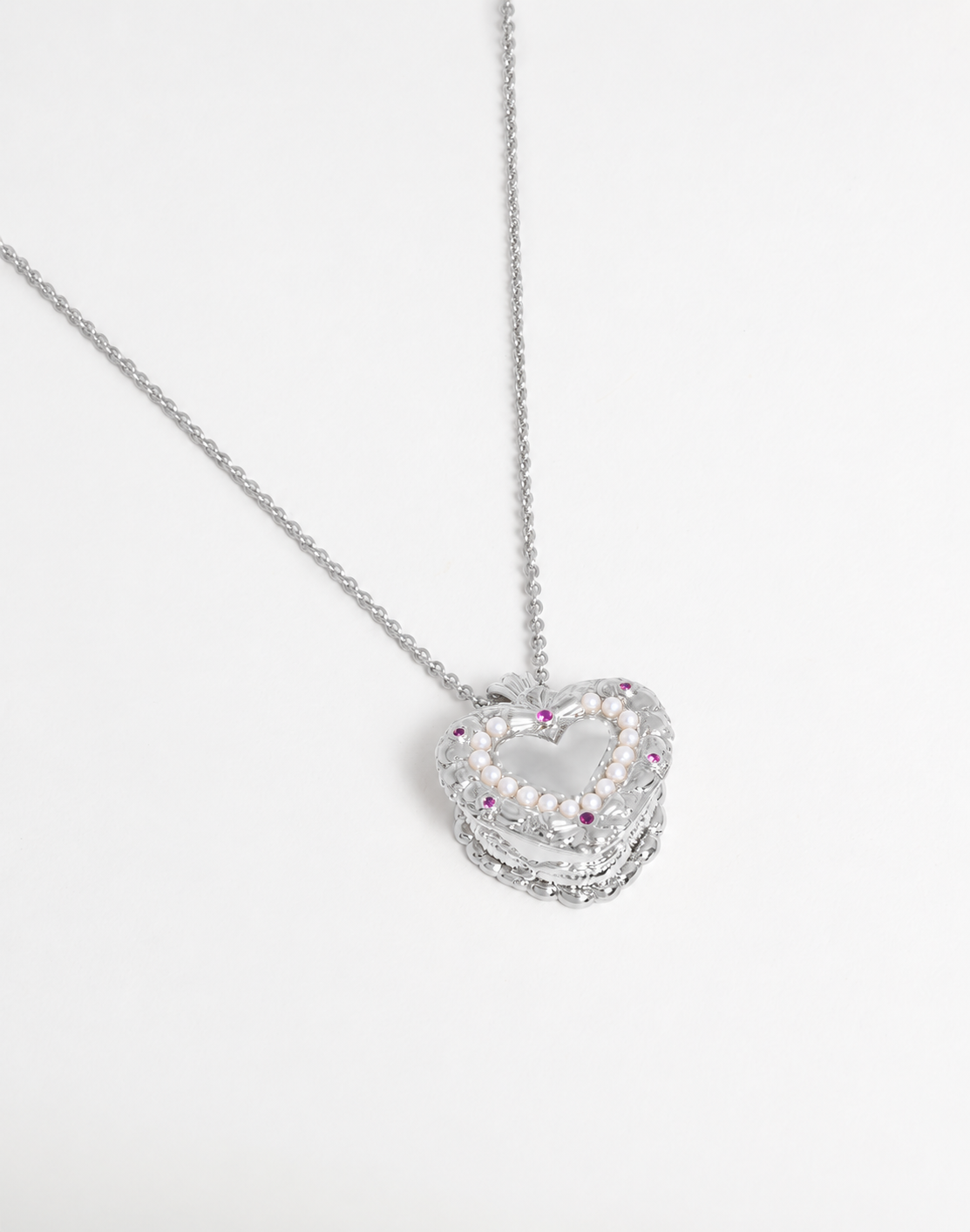 A silver-toned heart-shaped pendant necklace featuring a double-layered design with small white pearls and pink gemstone accents, displayed on a clean white background.