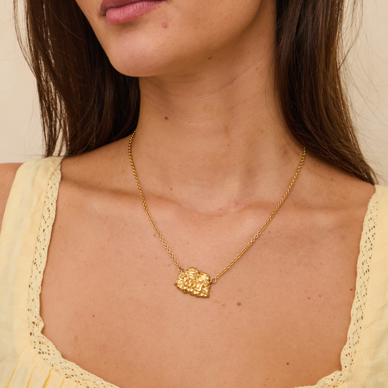 Close-up of a person wearing a gold necklace with a heart-shaped pendant.